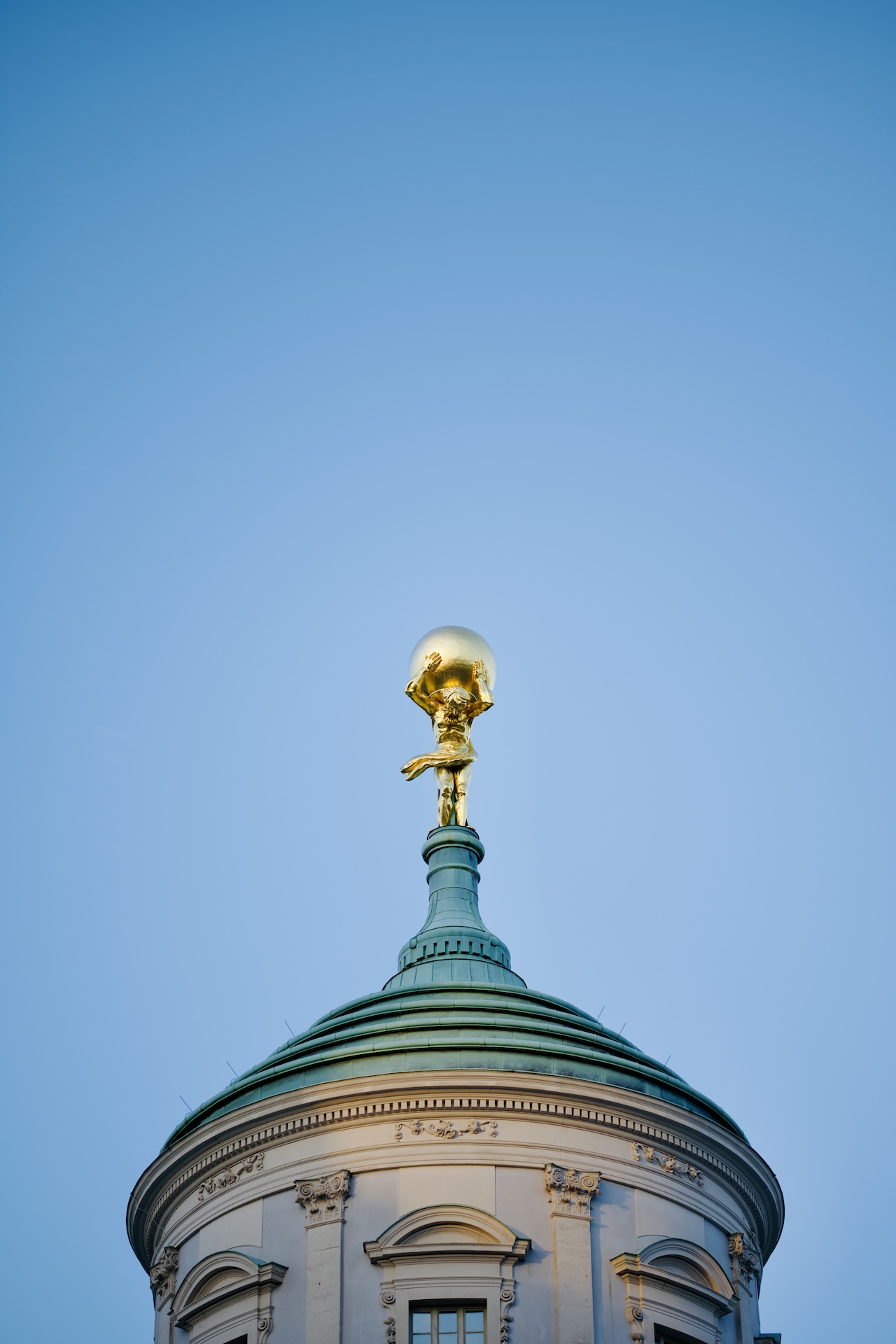 Goldene Figur auf einer Kuppel vor blauem Himmel.